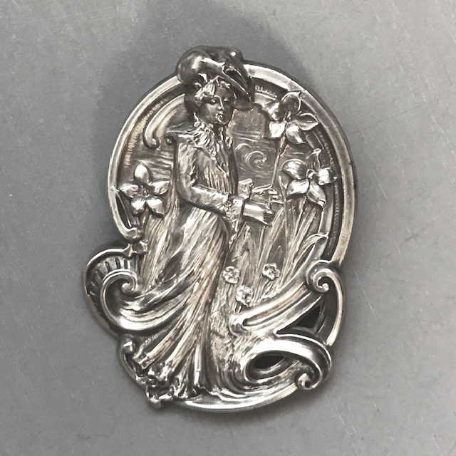 VICTORIAN sterling silver brooch with embossed lady in a garden of flowers, punched star mark and the words “sterling front” on the back