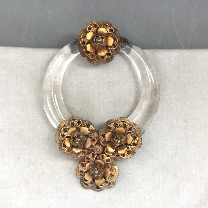 DEROSA dress clip of a clear glass circle with a faceted edge and multi-layered brass flowers, each with a bead center